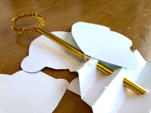 The paper angel craft is turned over to glue the angel wings onto the back of the gold paper straw running through the decoration. 
