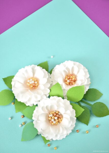 Three small white paper dahlia flowers with pearl centers. Each flower has small green leaves.